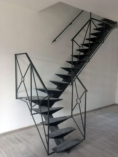 Escalier moderne en métal noir à marches flottantes et balustrades géométriques, dans un intérieur blanc minimaliste.