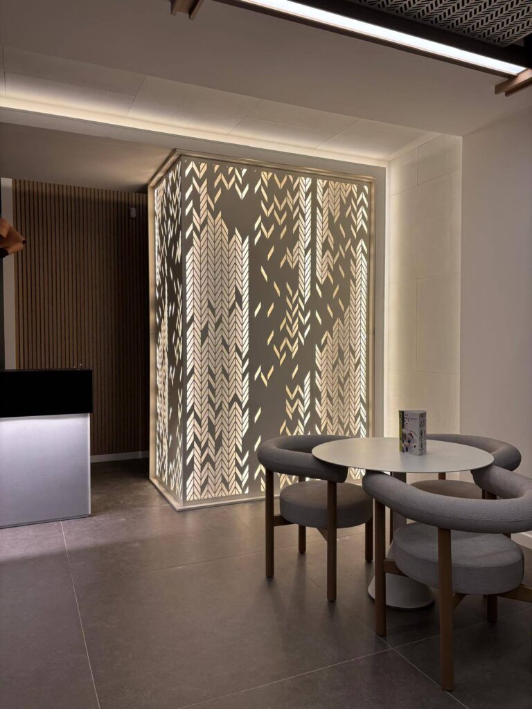 Design d'intérieur moderne avec paravent rétroéclairé Coin café design avec table ronde, chaises grises et paravent rétroéclairé au motif d'épis de blé stylisés.